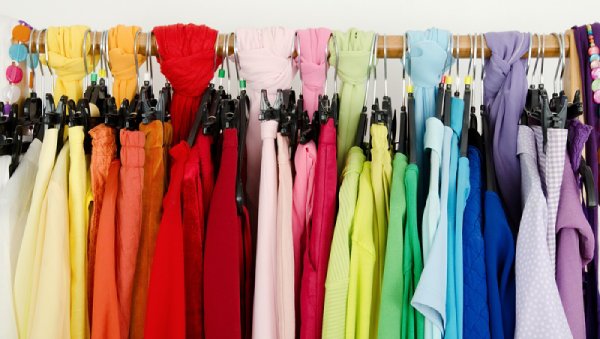 چندین لباس با رنگ تابستانی چیده شده در رگال کنار هم که به شکل رنگین کمان درآمده است.