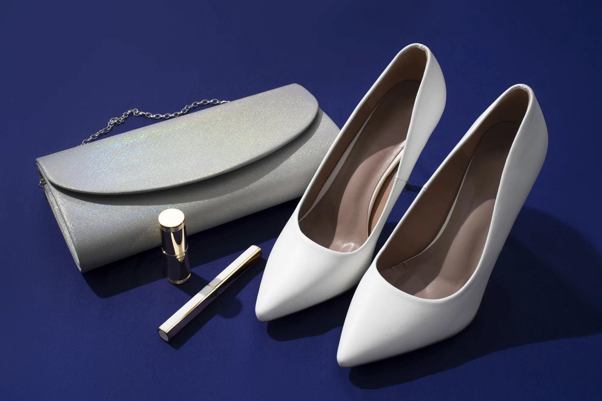 یک عدد کفش مجلسی برای مزون لباس زنانه کنار کیف مجلسی زنانه که روی یک صفحه بنفش قرار گرفته است.
